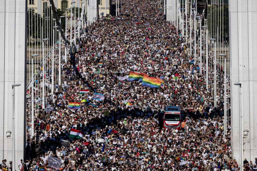 Sokszínű LGBTQ+ zászlók és tömeg a hidakon, balkáni ünnep vagy megemlékezés, beáramlás a kereszteződésbe.