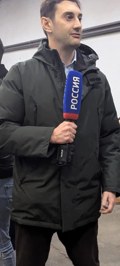 Fiatal férfi újságíró a városban, mikrofont tart a kezében.